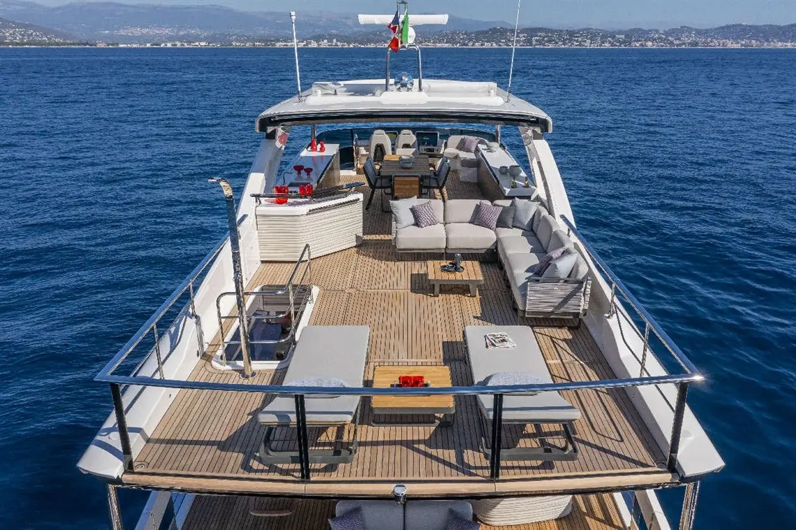 Luxury yacht deck featuring comfortable seating, a dining area, and scenic ocean views under clear skies.